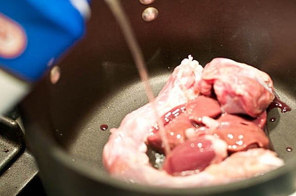 Giblets and neck of turkey shown in a medium saucepan with chicken broth being poured into the pan. // addapinch.com