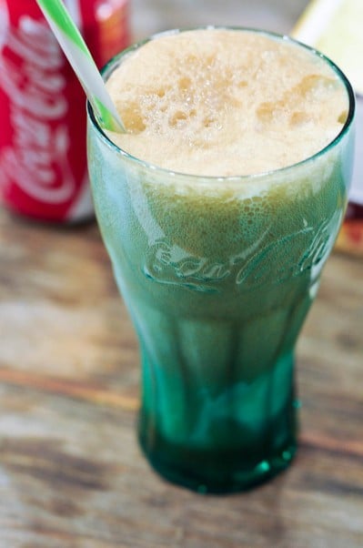 Coke float in a green glass coke glass with a straw and red and white Coke can in the background.