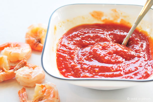 Cocktail Sauce in white blue rimmed bowl surrounded by boiled shrimp 