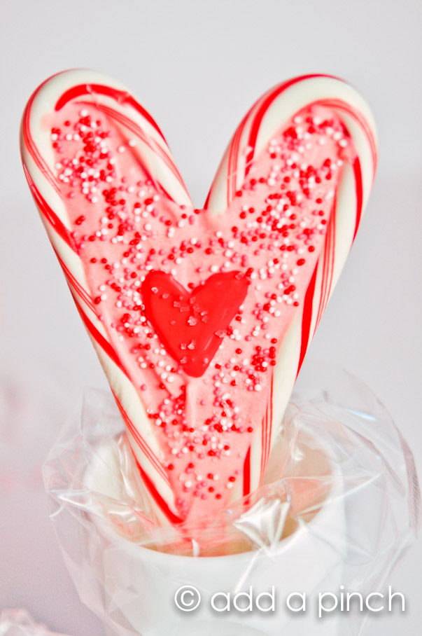 Photo of candy cane heart shaped lollipop in a white cup with cellophane.