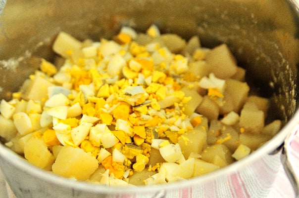 Potato salad ingredients of chopped cooked potatoes and diced hardboiled eggs ready to combine, in stainless pot. // addapinch.com