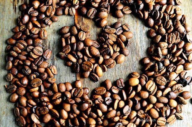 Whole espresso beans make a heart shape on a wooden board. 