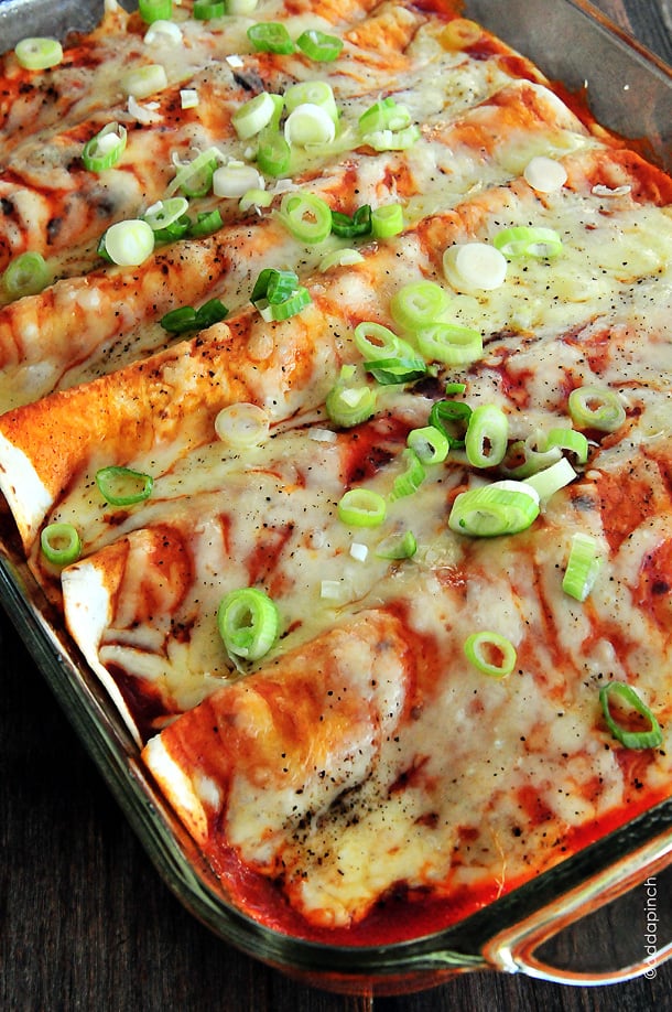 Baking dish of enchiladas covered in melted cheese and enchilada sauce and garnished with green onions - from addapinch.com