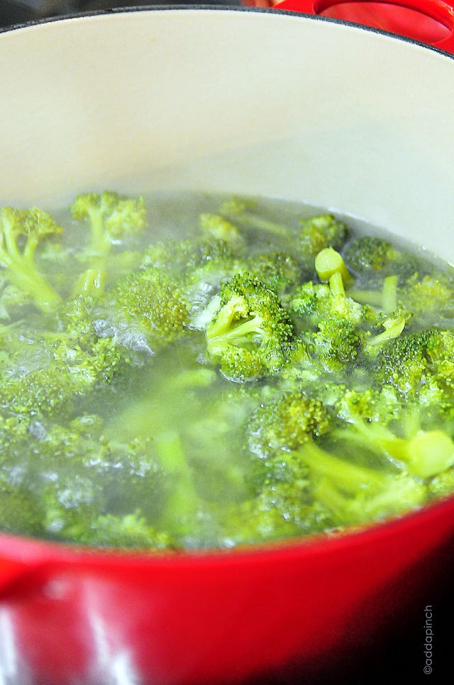 Red pot filled with broccoli florets cooking on the stove. 