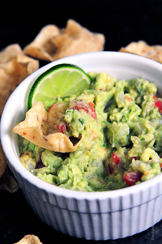 White dish of guacamole with a lime slice and a tortilla chip.