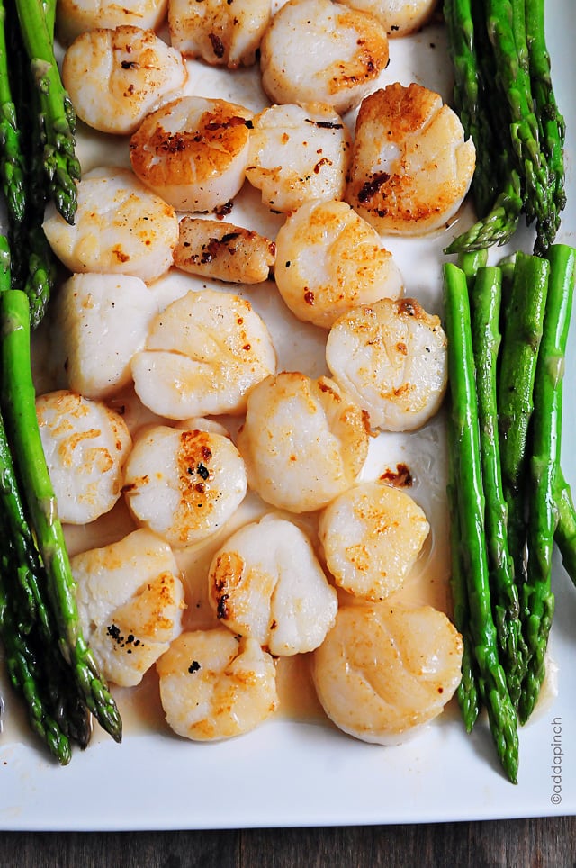 Overhead photograph of seared scallops and asparagus on a white platter. // addapinch.com
