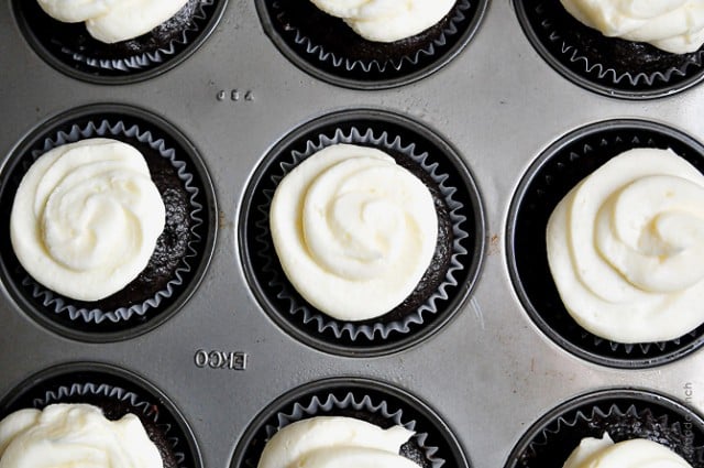 Rich chocolate cupcakes in a muffin tin topped with vanilla buttercream swirls.