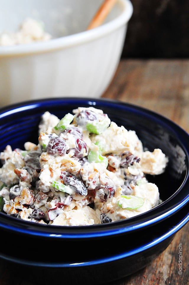 Photograph of chicken with grapes in a blue bowl on a wooden background. 