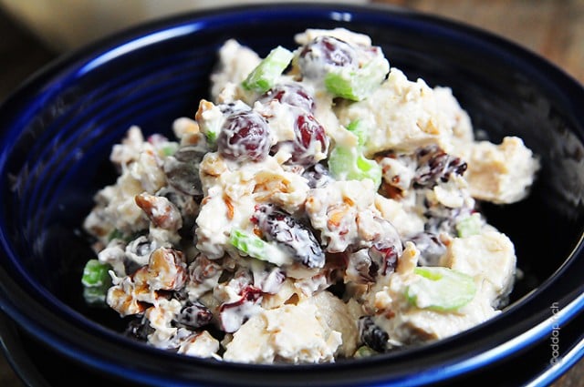 Photograph of chicken salad with grapes, celery and raisins in a blue bowl on a wooden background. 