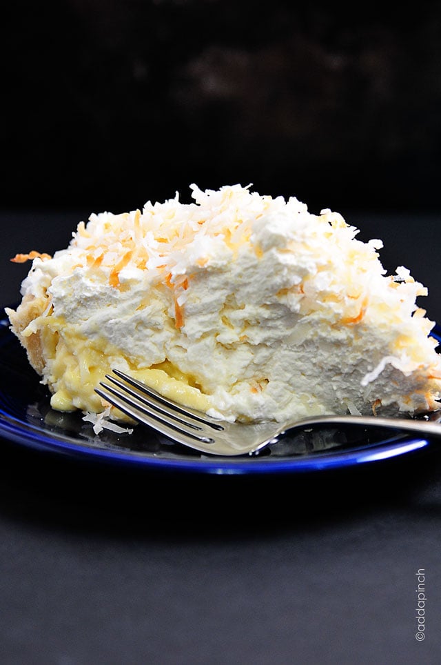 Side view of blue plate holding coconut cream pie, with thick coconut custurd and pillowy homemade whipped cream. 