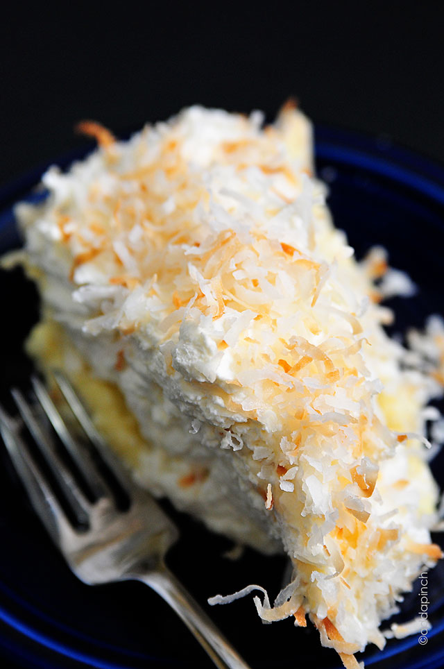 Closeup of blue plate and fork with Coconut Cream Pie covered in toasted coconut on top of thick whipped cream. 