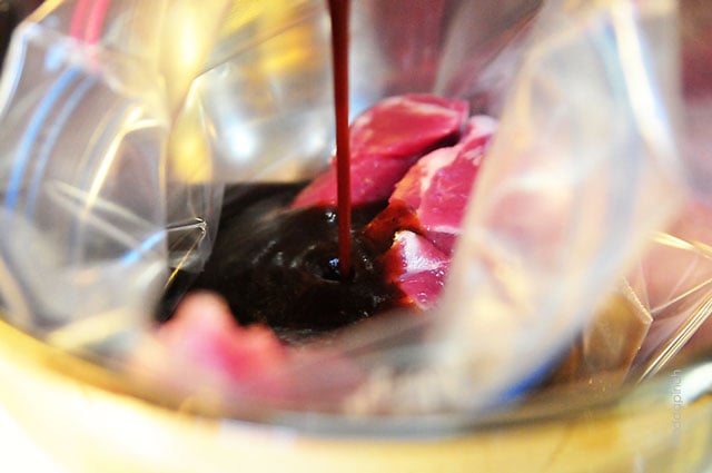 Marinade being poured into a zip-top bag filled with pork tenderloin.