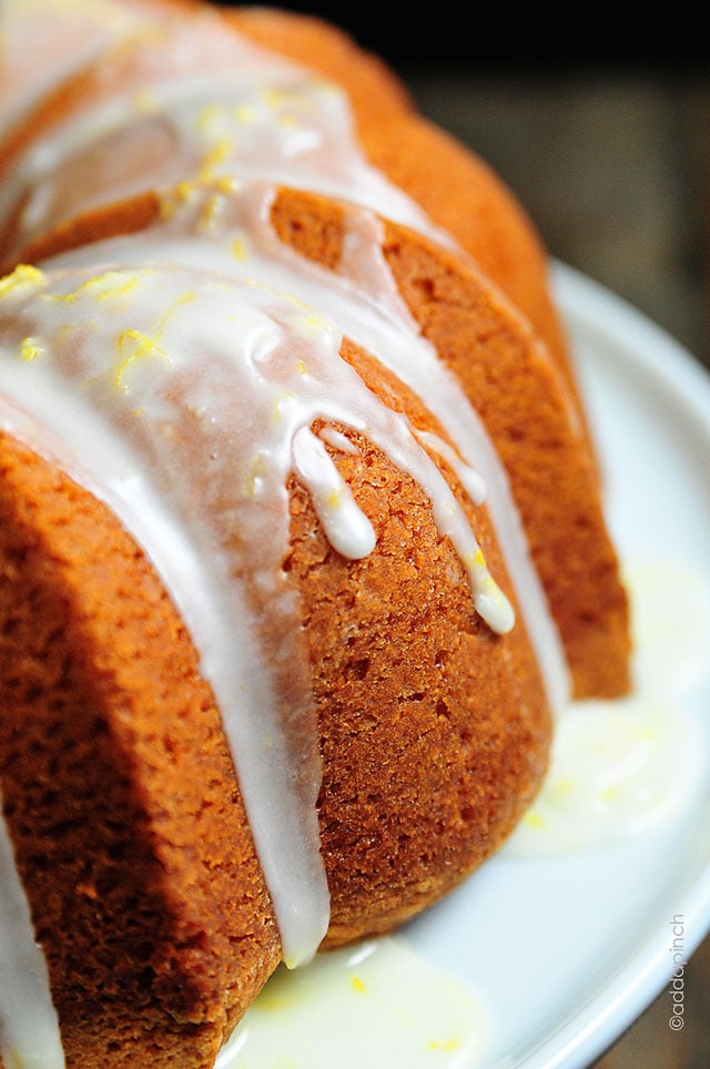 Side view of pound cake baked in bundt pan that is drizzled with a lemon glaze on a white plate 
 - // addapinch.com