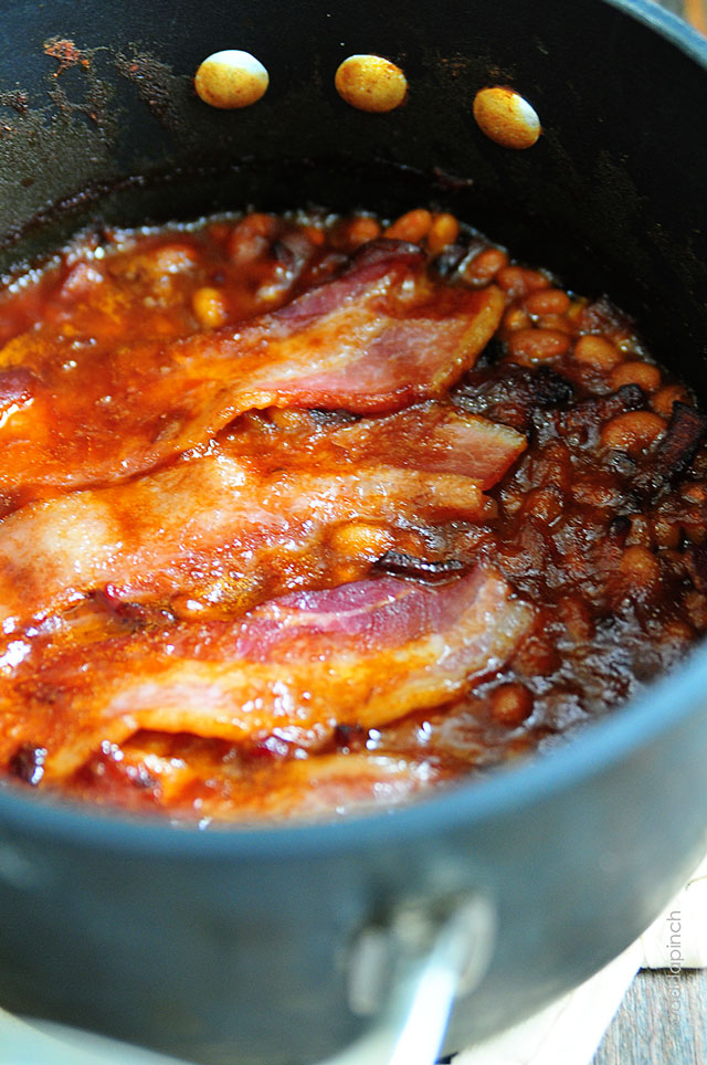 Cast iron dutch oven with cooked Southern Baked Beans topped with crispy bacon // addapinch.com