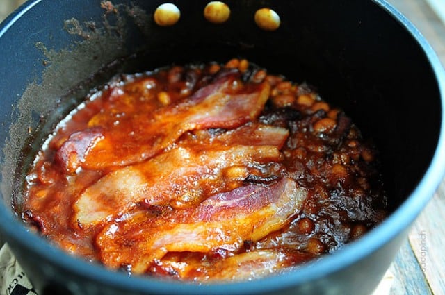 Dark stock pot filled with Baked Beans topped with slices of bacon  // addapinch.com