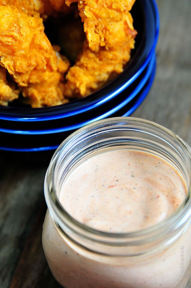 Chicken tenders in a blue bowl beside a clear glass bowl of comeback sauce.