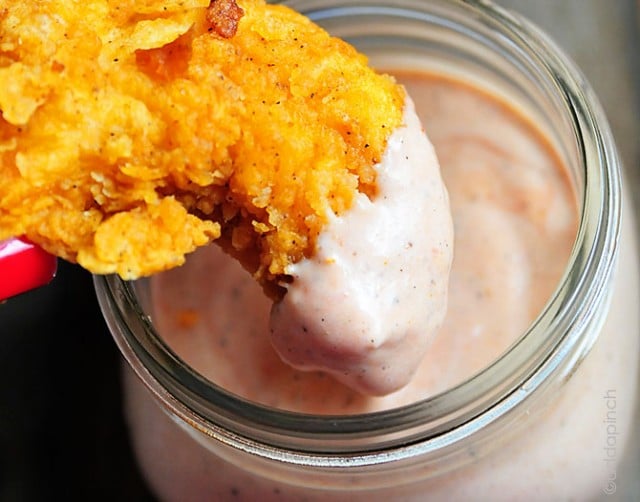 Chicken tender dipped into a glass container filled with comeback sauce.