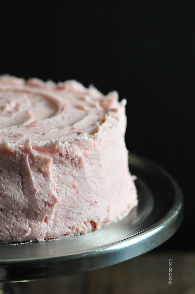 Cake frosted with Strawberry Buttercream Frosting on a pewter cake stand. 