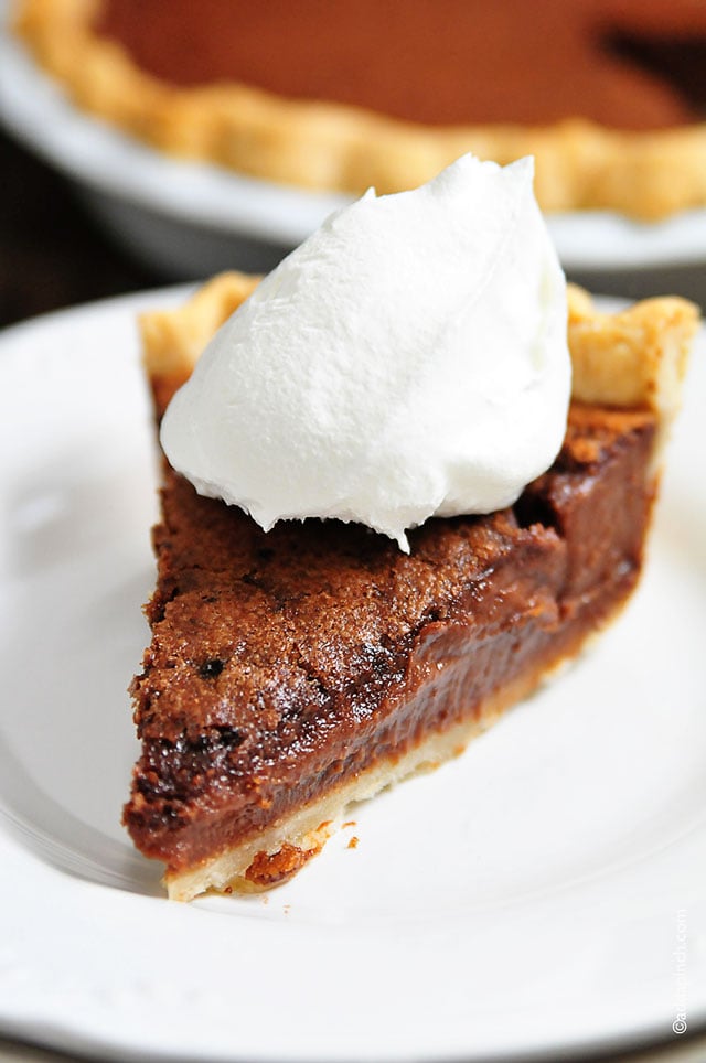 Photograph of slice of chocolate pie topped with whipped cream and full pie in the background. // addapinch.com