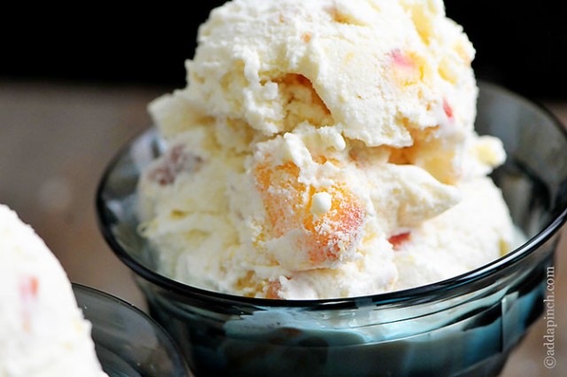 Two glass dishes of peach ice cream loaded with pieces of peaches visible. - ©addapinch.com