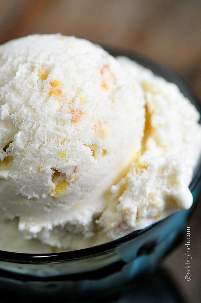 Blue glass bowl holds scoop of peach ice cream with visible bits of peaches - ©addapinch.com