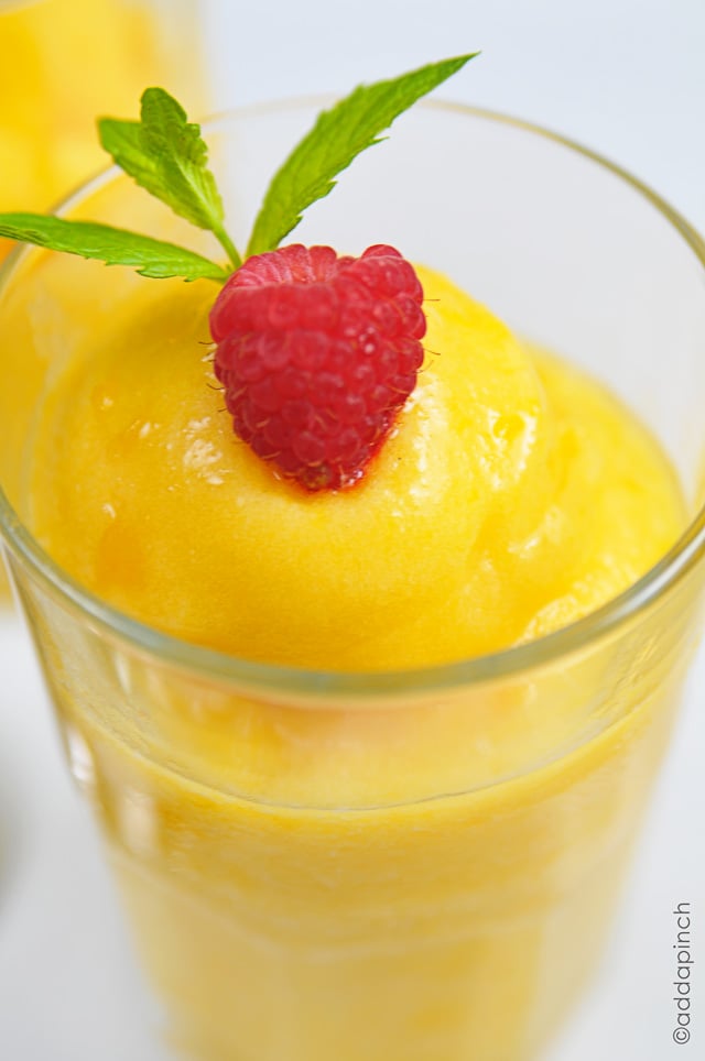 Peach sorbet in a glass topped with a fresh raspberry and sprig on mint.