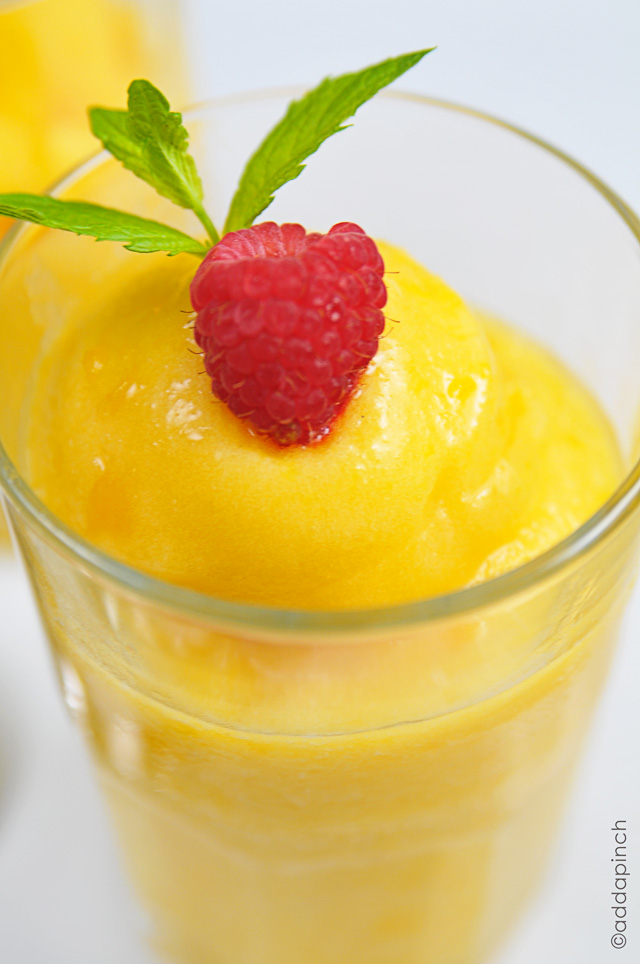 Peach sorbet in a glass topped with a fresh raspberry and sprig on mint.