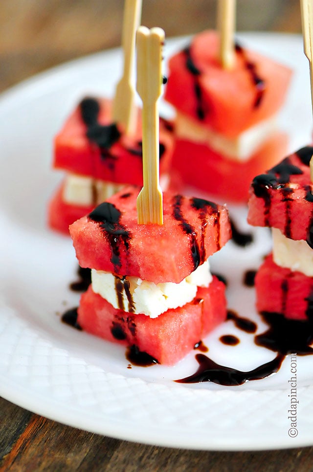 White plate with four watermelon feta appetizer bites topped with balsamic glaze // addapinch.com