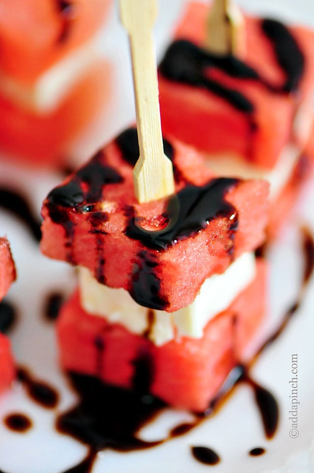 Cocktail skewer holds layer of two pieces of watermelon with cube of feta cheese in between. Drizzled with balsamic glaze and served on white plate // addapinch.com