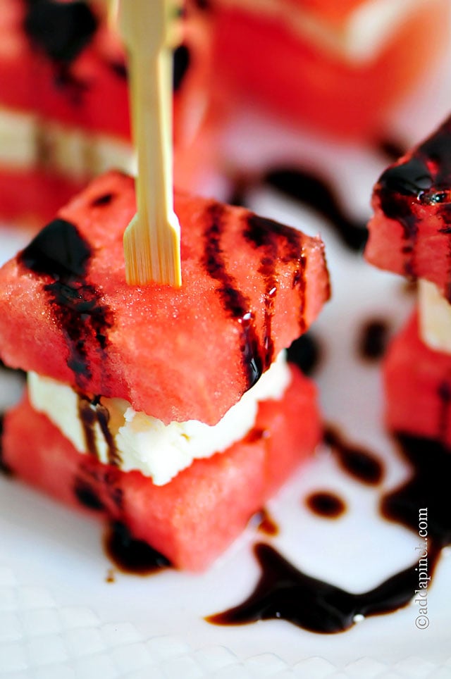 Close up of watermelon feta appetizer skewered with a wooden toothpick and drizzled with balsamic glaze //addapinch.com