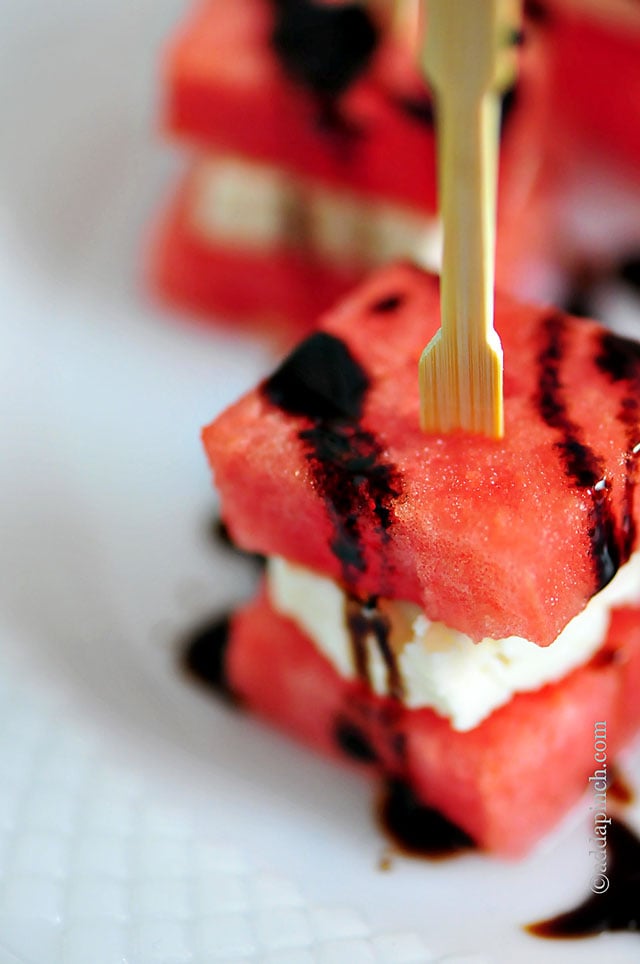 Juicy watermelon appetizer held with wooden toothpick and drizzled with balsamic glaze - on a white serving dish // addapinch.com