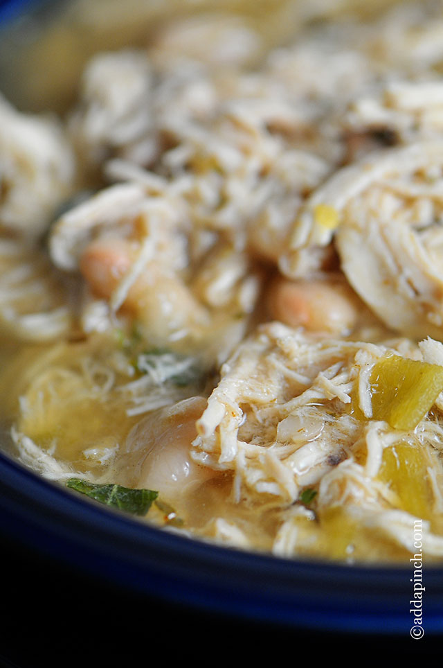 Chicken Chili showing white meat chicken, white beans and broth, in a blue bowl // addapinch.com