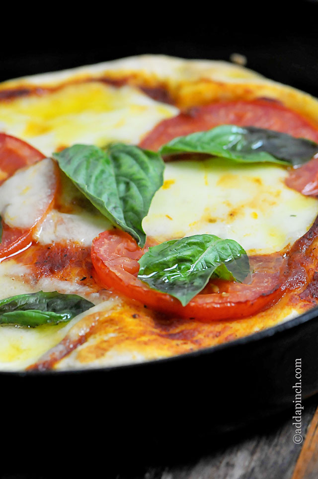 Margherita pizza topped with melted mozzarella, tomato sauce, fresh tomato slices and fresh basil all in a pizza pan. 