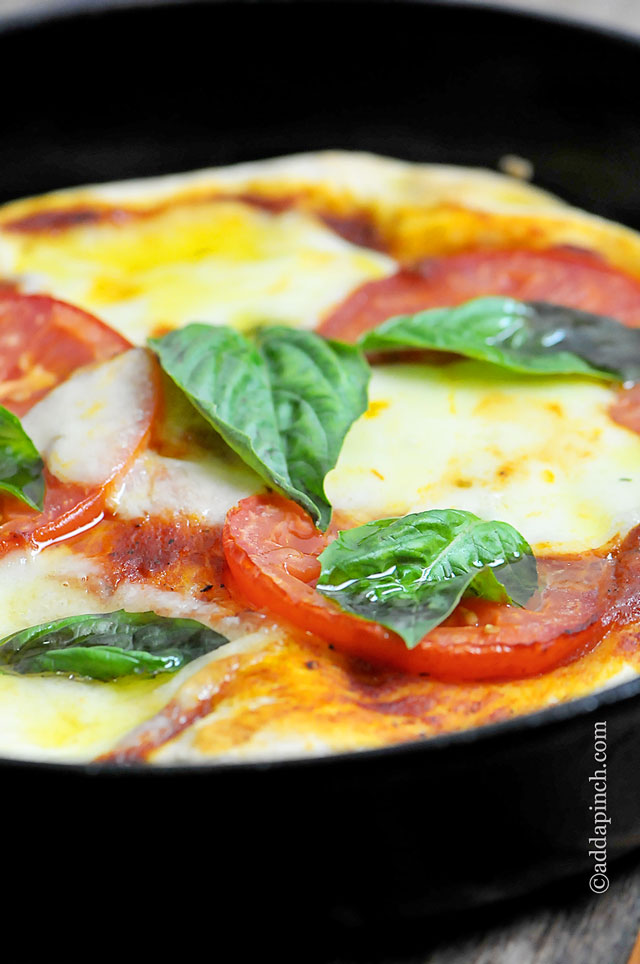 Skillet holds cheesy pizza with tomatoes and fresh basil.