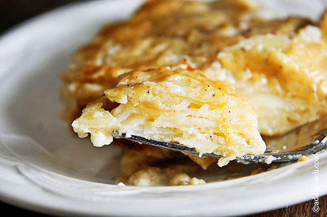 Horizontal photograph of scalloped potatoes on a fork on a white plate. // addapinch.com