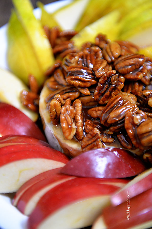 Pecan Praline Sauce is drizzled over warm brie and red and green apple slices in a circular arrangement. - addapinch.com