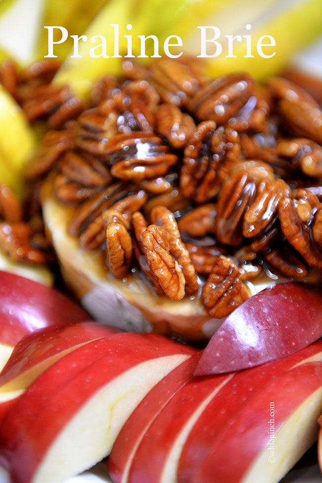 Close up photo of sliced red and green apples surrounding melty warm brie, all topped with pecan praline sauce - addapinch.com