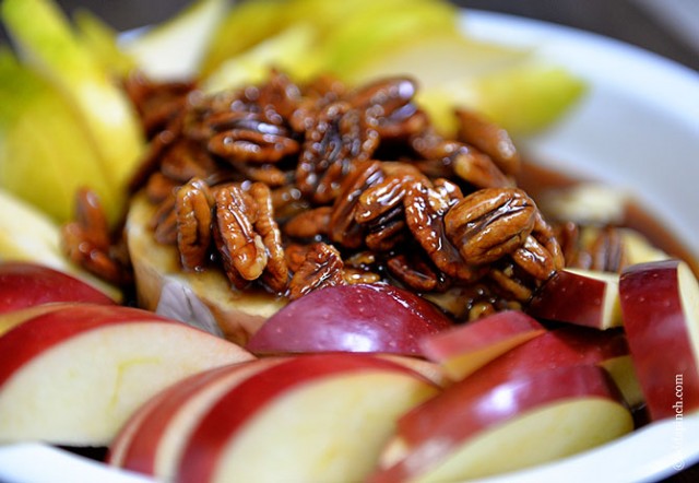Apple slices surround warm brie topped with pecan praline sauce on a plate - addapinch.com