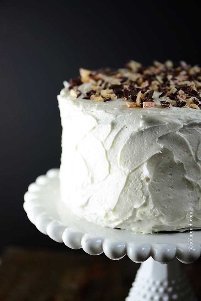 Side view of cake topped with peppermint bark on white antique cake stand. 