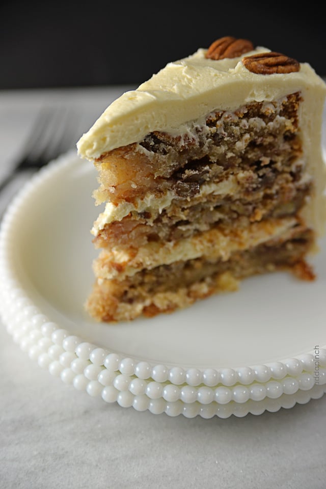 Closeup photo of a slice of Hummingbird Cake, showing pecans, pineapple  and cream cheese frosting. 