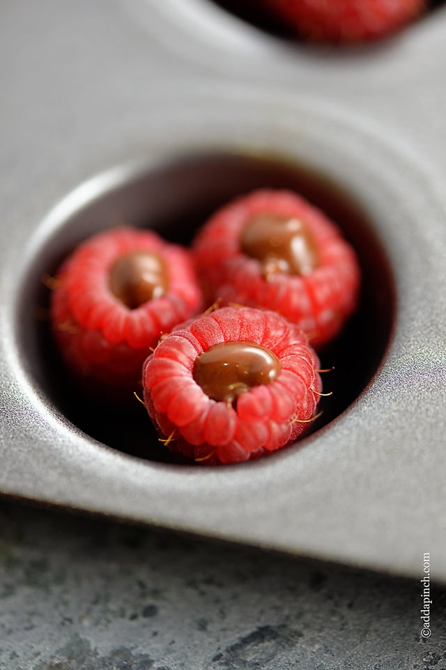 Muffin pan holds raspberries that have been freshly filled with chocolate. 