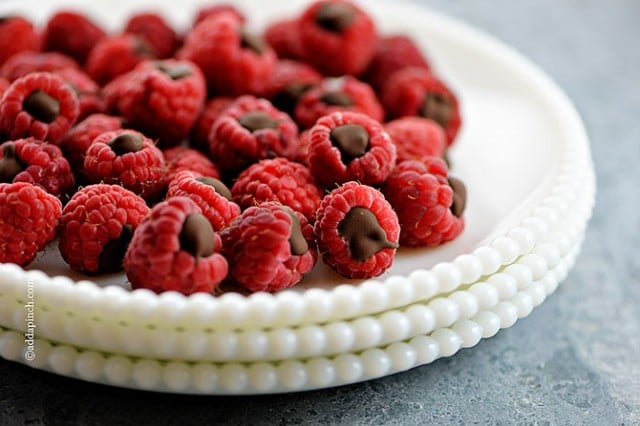 White scalloped edge plates are stacked and filled with raspberries filled with chocolate. 