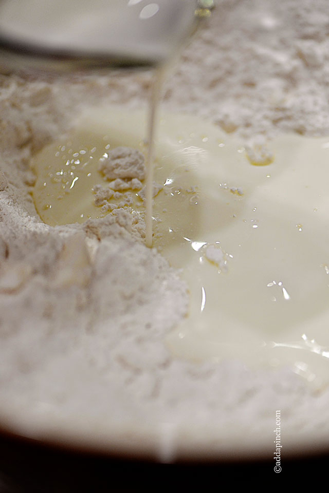 Closeup of flour that has had the shortening cut into the mixture for Three Ingredient Buttermilk Biscuits with buttermilk being slowly added - ©addapinch.com