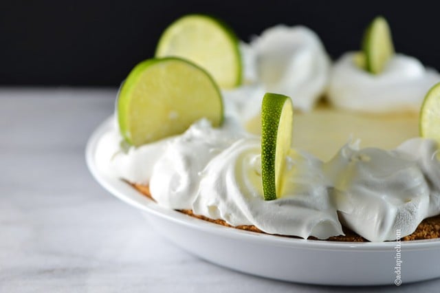 Side view of pie on marble counter with lime slices standing in clouds of whipped cream. 