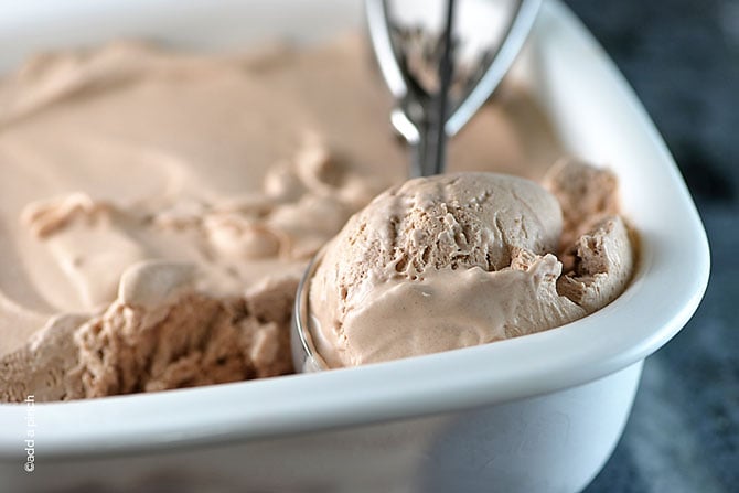 White dish holds creamy chocolate ice cream with an ice cream scoop dipping out a scoop. // addapinch.com