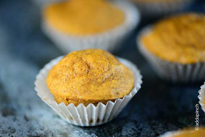 Close side view of pumpkin muffins in paper muffin liners on granite countertop. 