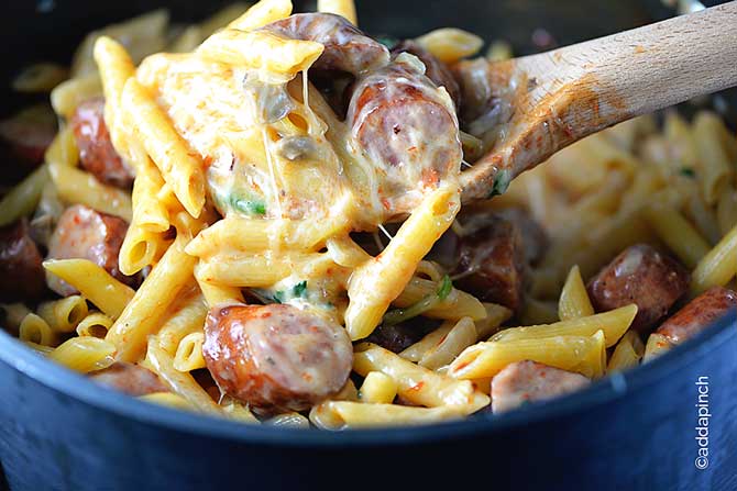 Pot with penne pasta, slices of sausage, spinach, and melted strings of cheese. 