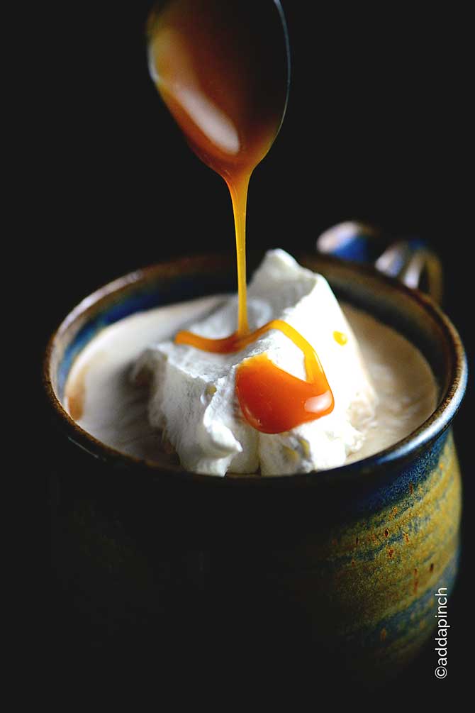 Salted Caramel Mocha Recipe with dollop of whipped cream on top, with caramel being drizzled with a spoon on top. // addapinch.com