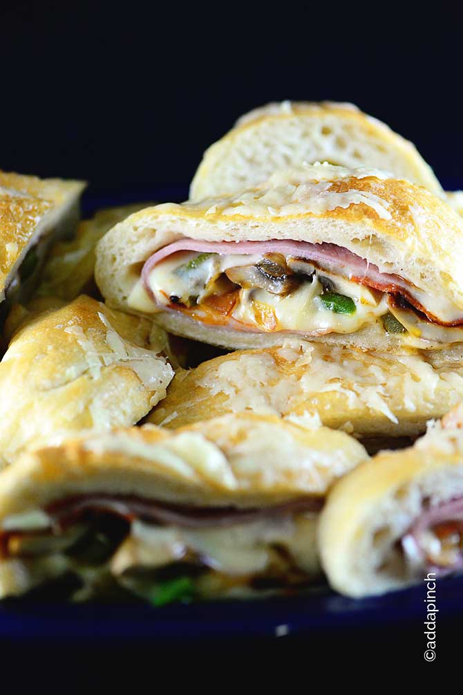 Stromboli stacked on a blue platter. Covered in cheese and filled with meat, melted cheese, mushrooms, peppers and more //addapinch.com