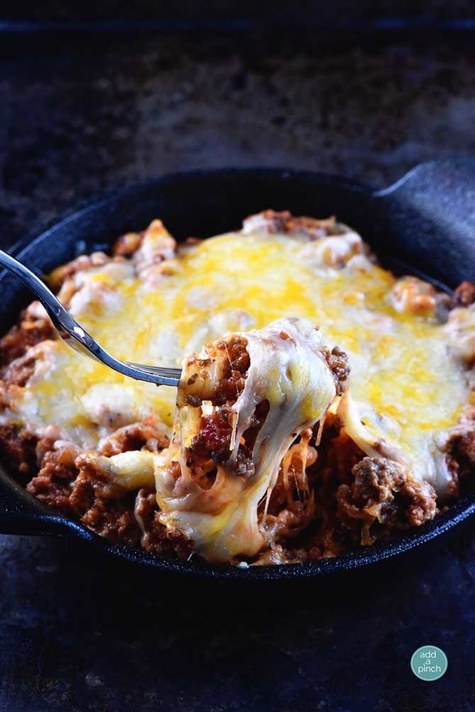 Baked spaghetti squash lasagna in a black dish with a scoop on a fork on a dark background.